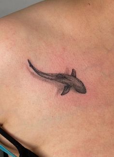 a small shark tattoo on the back of a woman's left shoulder and chest