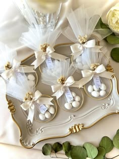 four small white candies in gold trays with ribbons and tags on them, surrounded by greenery