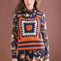 a woman is wearing an orange and blue crochet sweater with flowers on it