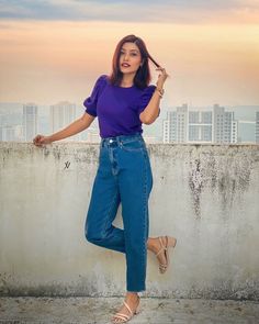 a woman standing on top of a cement wall with her hands in her hair and wearing blue jeans