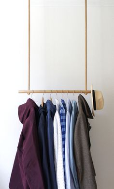 several shirts hanging on a clothes rack in front of a white wall and wooden hanger