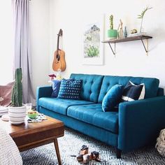 a living room with a blue couch and guitar on the wall next to a coffee table