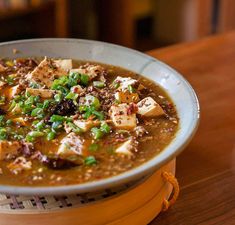 a bowl of soup with tofu, green onions and other toppings on a wooden table