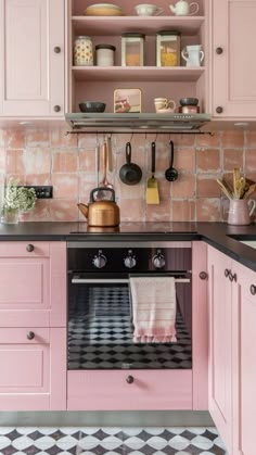 a pink kitchen with black and white checkered flooring on the walls, cupboards and shelves