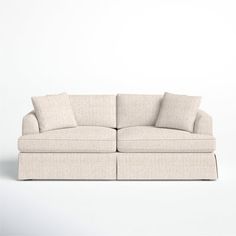 a white couch sitting on top of a white floor next to a wall with two pillows