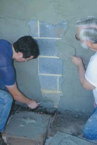 two men working on a wall with cement