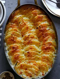 a casserole dish with potatoes and cheese in it on a table next to silverware