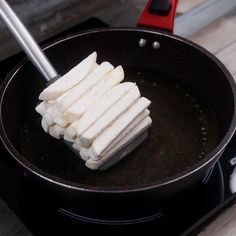 tofu being cooked in a frying pan with tongs on the burner