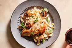 a plate with chicken, pasta and mushrooms on it next to a glass of wine