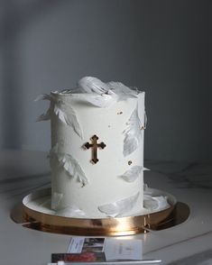 a wedding cake with white feathers and a cross on the top is sitting on a gold plate