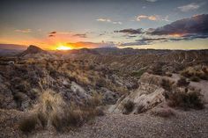 the sun is setting in the desert with mountains and scrubby grass on the ground