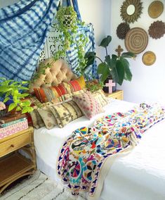 a bed covered in lots of pillows next to a wall with pictures on it and plants