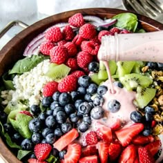 a wooden bowl filled with berries, blueberries and cucumber on top of a table