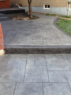 an outdoor patio with steps leading up to a tree in the back ground and grass on the other side