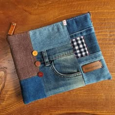 a small pouch made out of jeans with buttons on the front and back pocket, sitting on a wooden surface