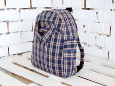 a blue and yellow plaid backpack sitting on top of a wooden bench in front of a white brick wall