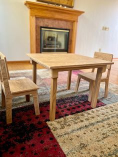 two wooden chairs sitting next to a table on top of a rug in front of a fireplace