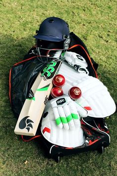 a helmet and some cricket equipment laying on the grass in a bag with it's contents