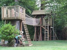 a man is working on a wooden play set in the yard with trees and bushes behind him