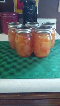 four jars filled with pickles sitting on top of a green tablecloth covered counter