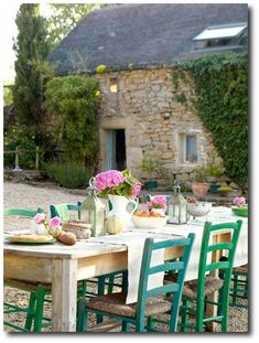 an outdoor dining table with green chairs and flowers in vases on the table outside