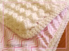 a crocheted blanket laying on top of a pink and white bedspread