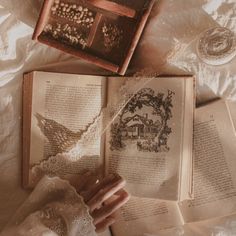 an open book on top of a bed next to two wine glasses and a lace doily