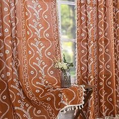 an orange curtain with white flowers on it and a chair in front of the window