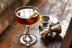 a drink in a glass with an orange peel on the rim sitting on a wooden table