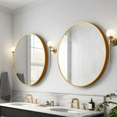 two round mirrors on the wall in a bathroom with marble counter tops and gold faucets