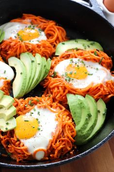 eggs and noodles in a skillet with avocado slices on the side for garnish