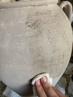 a person is holding something in their hand near a large clay pot on the ground