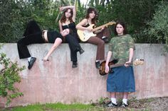 three young people are sitting on a wall with guitars and one is holding a guitar