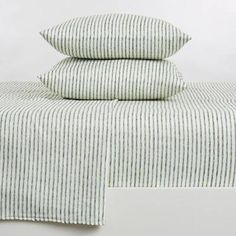 three pillows stacked on top of each other next to a bed with white and gray striped sheets