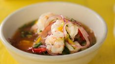 a white bowl filled with shrimp and vegetables on top of a yellow tablecloth next to a cup of soup