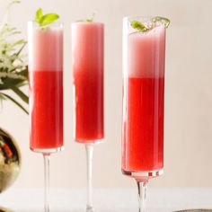 two tall glasses filled with red liquid and garnished with green leaves sit on a table