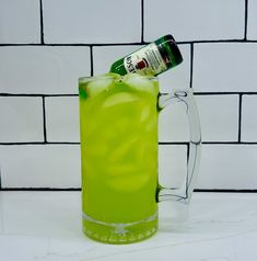 a green drink in a glass mug with a bottle on the top and white brick wall behind it