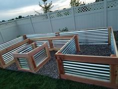 several wooden raised garden beds sitting on top of some gravel in the grass near a fence