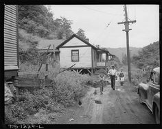 an old black and white photo of people walking down a dirt road in front of a house