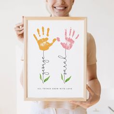 a woman holding up a framed print with two hands and the words, all things grow with love