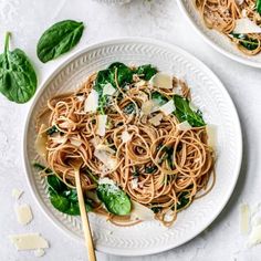 two white plates filled with pasta and spinach on top of a white tablecloth