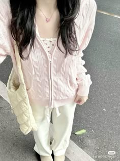 a woman with long black hair wearing pink sweater and white pants standing on the street