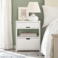 a white nightstand with two books on it next to a lamp and window sill