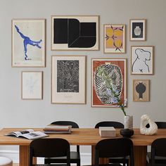 a wooden table topped with black chairs next to a wall covered in pictures and art