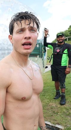 a man with no shirt on standing in front of a large bubble ball while another man holds his hand up