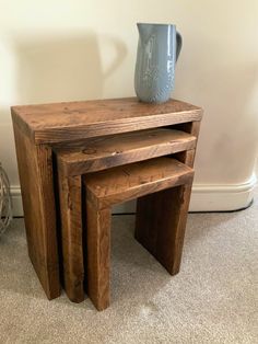 three wooden tables stacked on top of each other in front of a wall with a vase