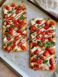 two square shaped pizzas with tomatoes and mozzarella on them sitting on a baking sheet