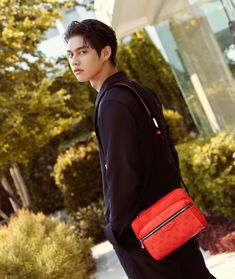 a young man is walking down the street carrying a red bag