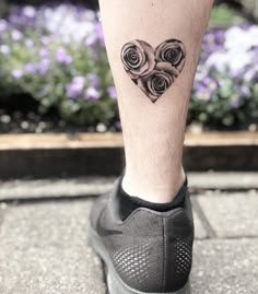 a woman's leg with a heart tattoo on it and flowers in the background