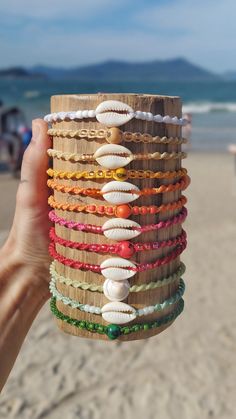 a person holding up a stack of bracelets on top of a sandy beach next to the ocean